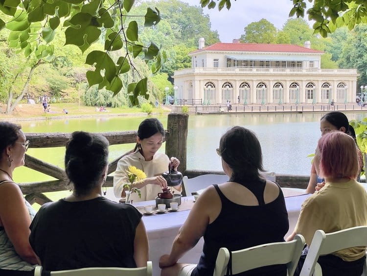 Six people seated enjoying tea outside on a sunny summer day.