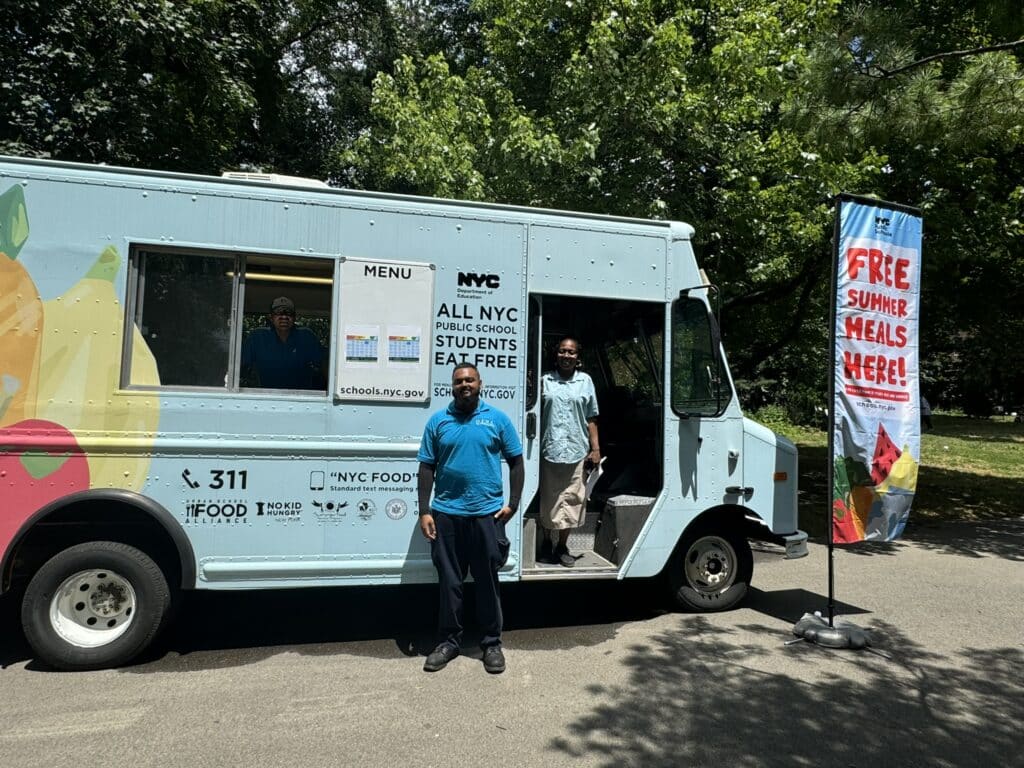 DOE employees standing within a food truck ready to serve summer meals