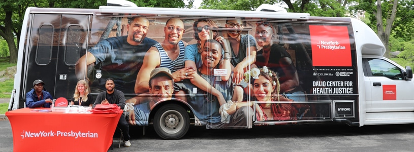 3 Heathcare workers on a table providing service in front of a New York Presbyterian mobile truck.