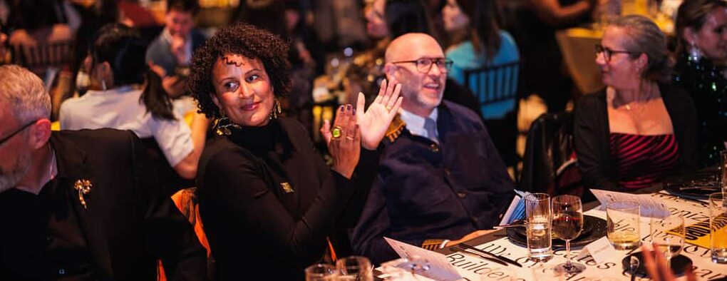 Morgan Monaco, a woman in a black turtleneck with curly hair, claps at a table at the BKO Changemakers ball