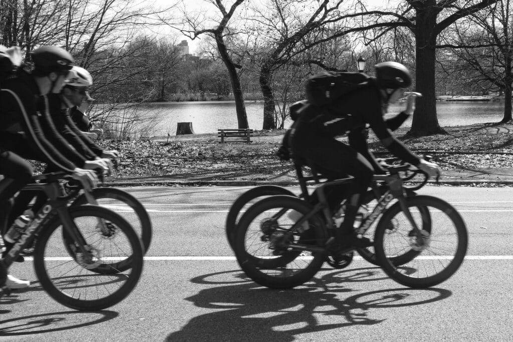 a black and white photo of people cycling in Prospect Park by the lake